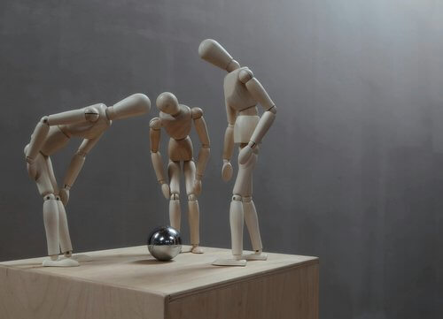 Drei h&ouml;lzerne K&uuml;nstlerpuppen b&uuml;cken sich &uuml;ber eine gl&auml;nzende Metallkugel auf einem Holzw&uuml;rfel.